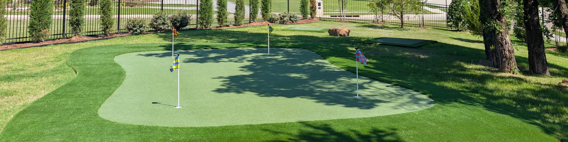 Multi-hole backyard putting green with fringe turf under a large shade tree